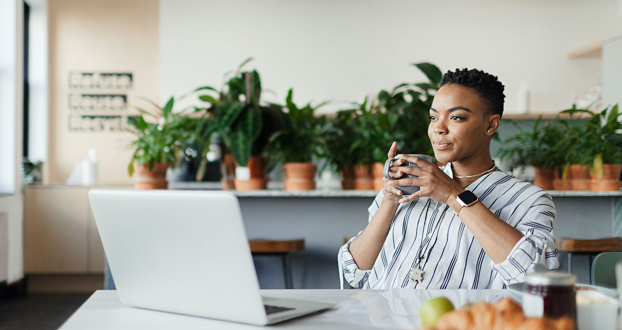 Woman drinking from a mug, sitting in front of a laptop simling