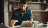 A man sitting at a table, holding a tablet and his debit card looking thoughtful