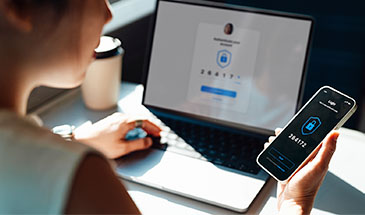 Woman sitting in front of a laptop, using her phone for secure login