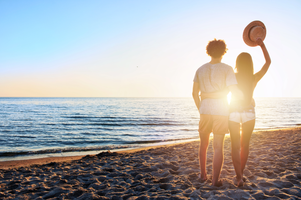 An image of a couple standing on a beach with the sun setting in front of them