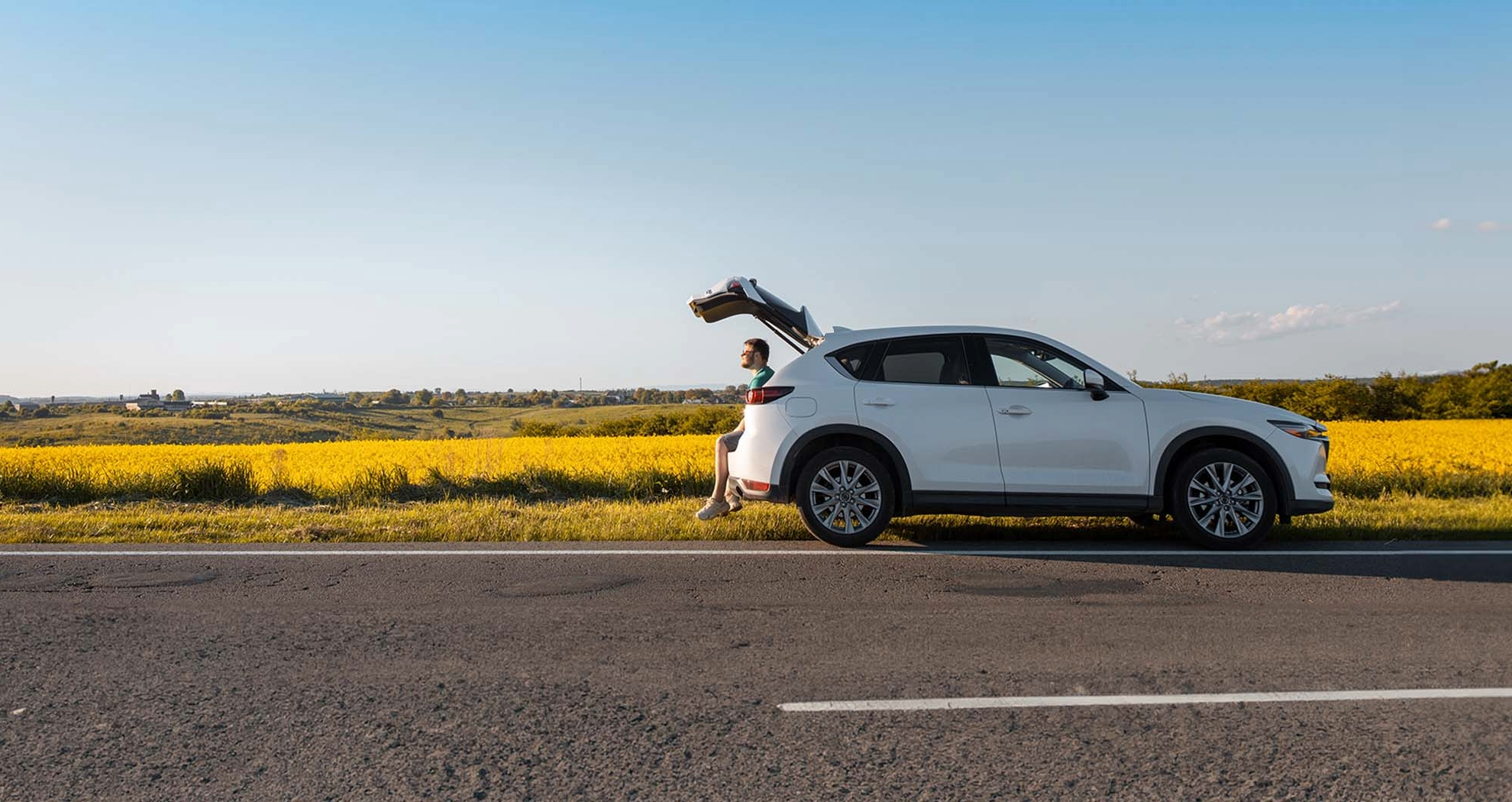 A car parked on a country roadside with a man sitting in the open boot 