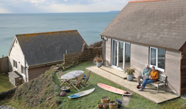 Two men sitting out front of a holiday home overlooking the sea