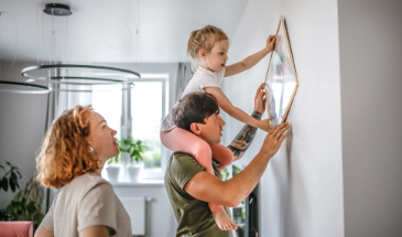 Young couple and child hanging pictures on their living room wall