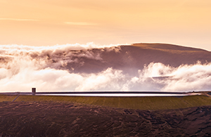 Pipeline with green field in foreground and mountain with low clouds in background