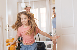 Little girl running into hotel room with parents wheeling suitcases behind her