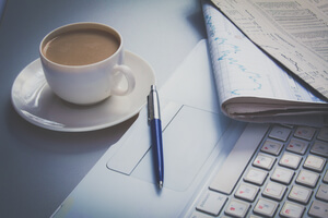 Clip board and cup of coffee beside laptop