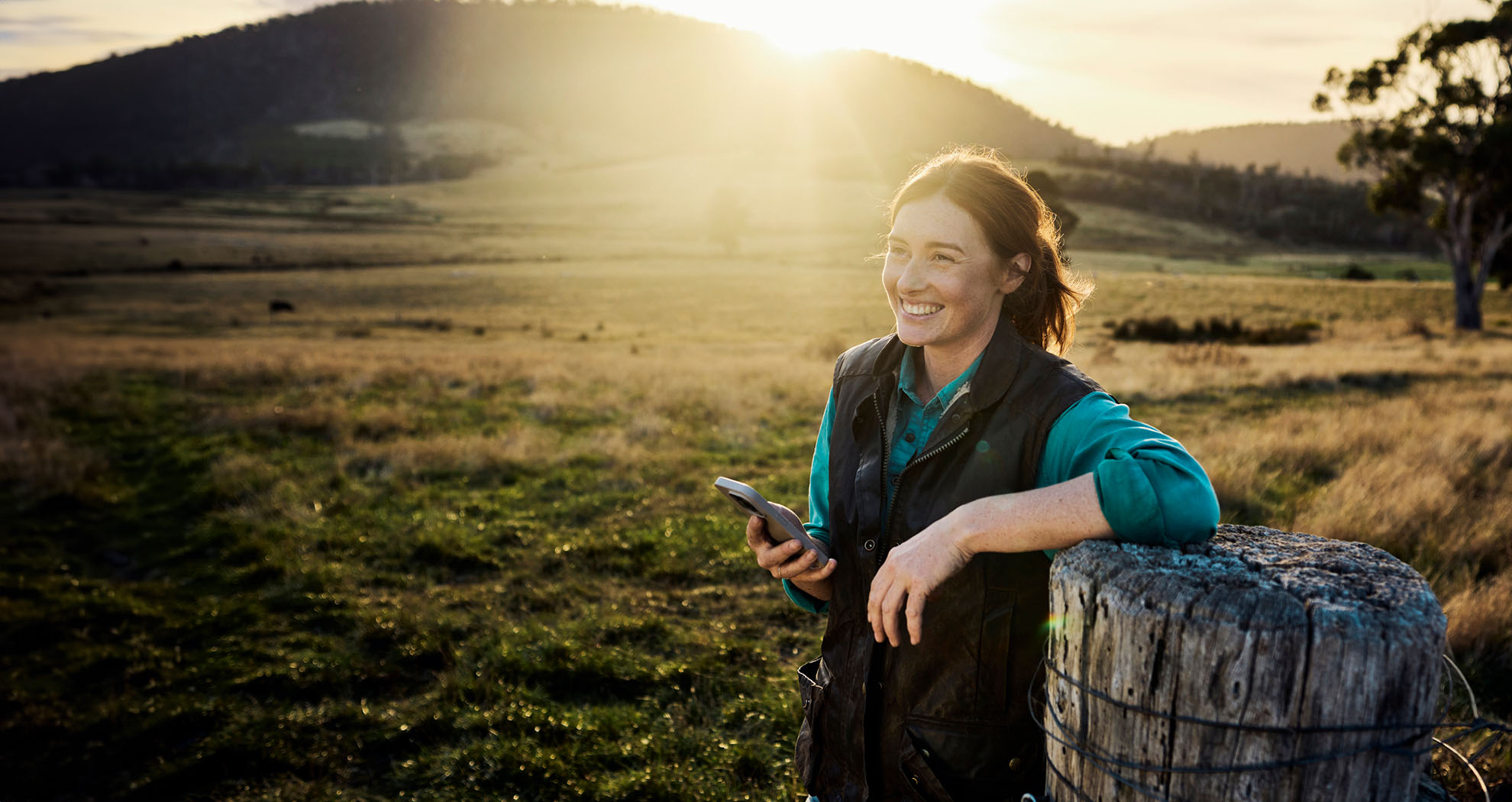 Woman smiling in a field holding her phone